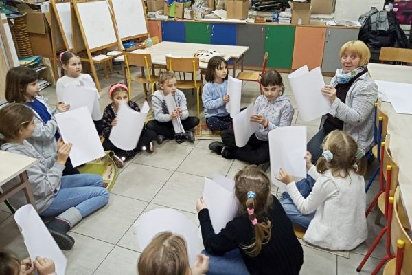 grupa dzieci w trakcie zajęć, trzymają w rękach kartki papieru