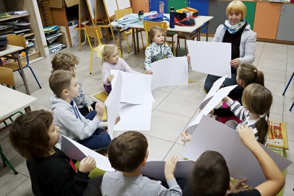 grupa dzieci w trakcie zajęć, trzymają w rękach kartki papieru