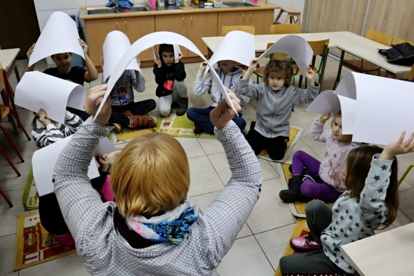 grupa dzieci w trakcie zajęć, trzymają w rękach kartki papieru
