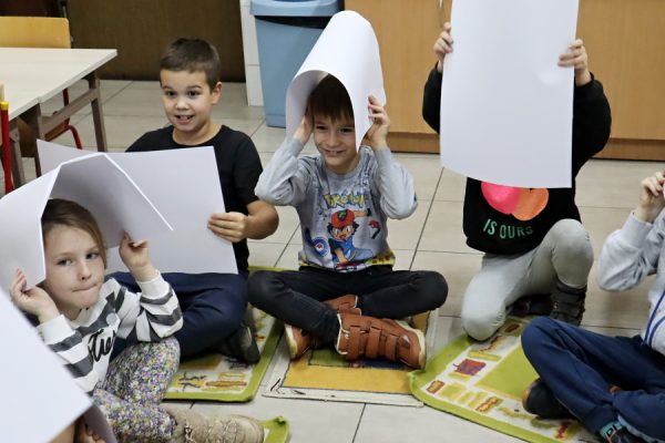 grupa dzieci w trakcie zajęć, trzymają w rękach kartki papieru