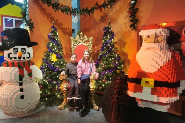 dwójka dzieci pozuje do zdjęcia wokół dwie choinki i bałwanek z mikolajem z klocków Lego