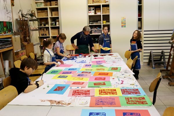 uczestnicy z nauczycielką stoją przy stole pełnym graficznych odbitek