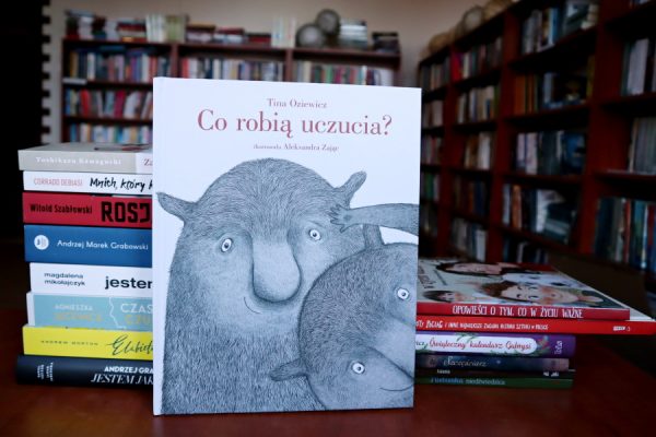 książka "Co robią uczucia" w tle regały biblioteczne