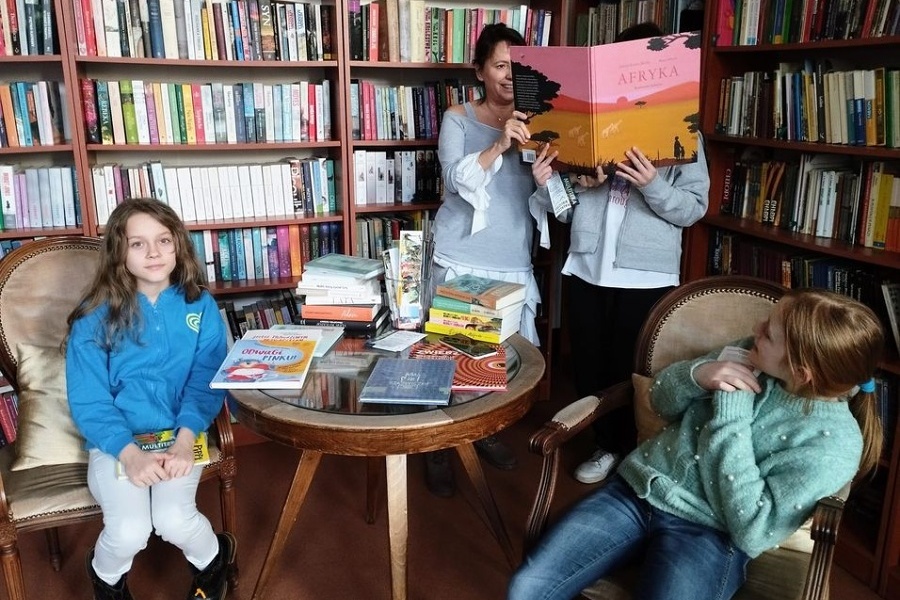 dwieczynki z nauczycielką w bibliotece, trzymają książkę o Afryce