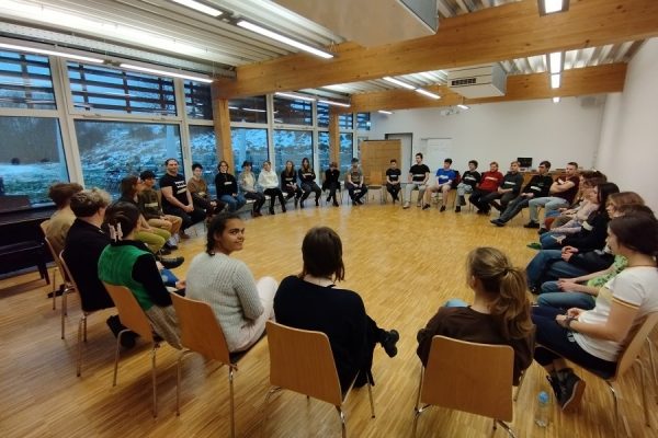 grupa młodzieży siedzi w kole na krzesłach