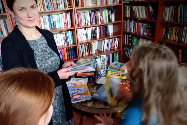 dwie dziewczynki z kobietą, w tle regały z książkami