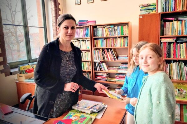 dwie dziewczynki z kobietą, w tle regały z książkami