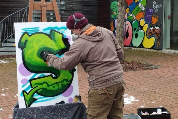 artysta w trakcie tworzenia sprayem litery S