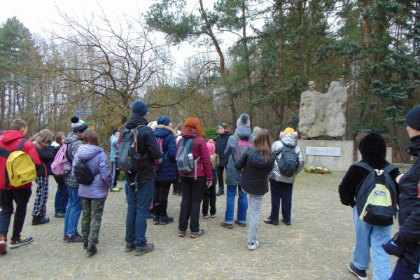 grupa młodzieży stoi przed kamiennym pomnikiem ofiar hitleryzmu w Trzeszczynie