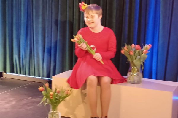 uczestniczka siedzi trzyma kwaity obok wazony z kwiatami