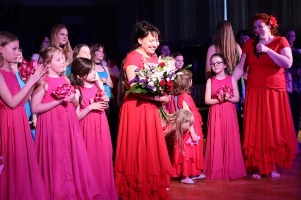 kobieta z kwiatami za nią dziewczęta w barwnych strojach