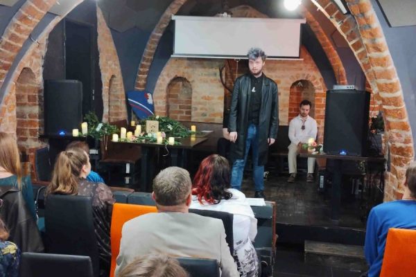 publiczność zgromadzona na wydarzeniu, na scenie osoba występująca