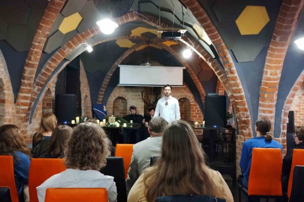 publiczność zgromadzona na wydarzeniu, na scenie osoba występująca