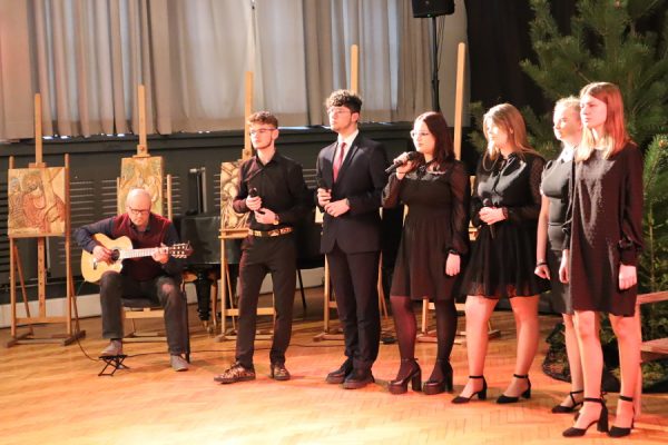 grupa młodzieży w trakcie występów mężczyzna siedzi na krześle z gitarą