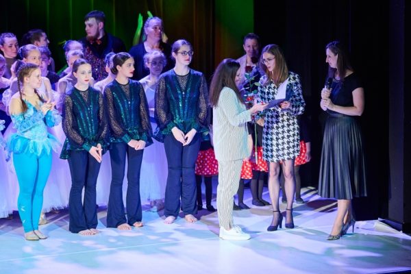 grupa dziewcząt na scenie nauczycielka odbiera statuetkę