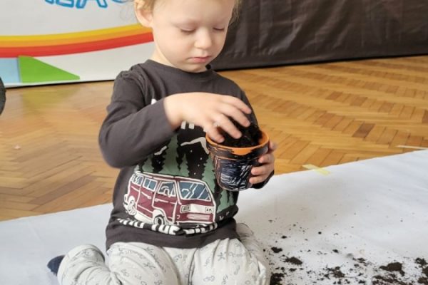 chłopiec sypie ziemię do doniczki