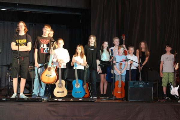 grupa dzieci i młodzieży na scenie obok nich gitary