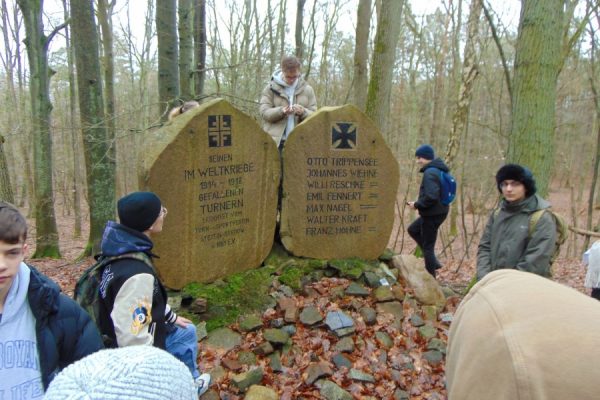 kamienny pomnik sportowców, obok młodzież, w tle las