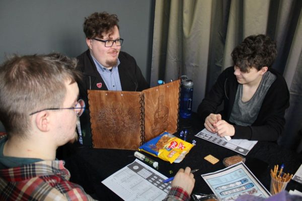 trzy osoby siedzą przy stole i grają