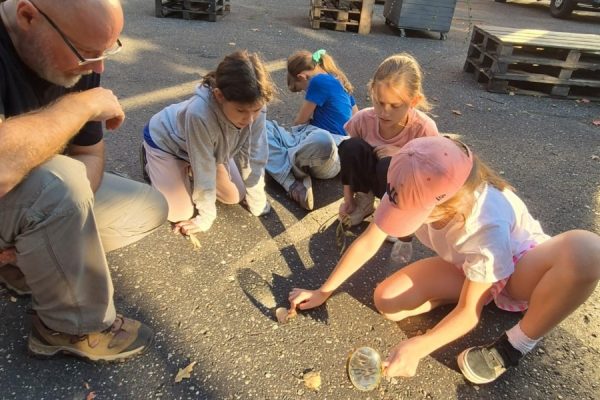 grupa dzieci z nauczycielem na boisku, dzieci mają lupę