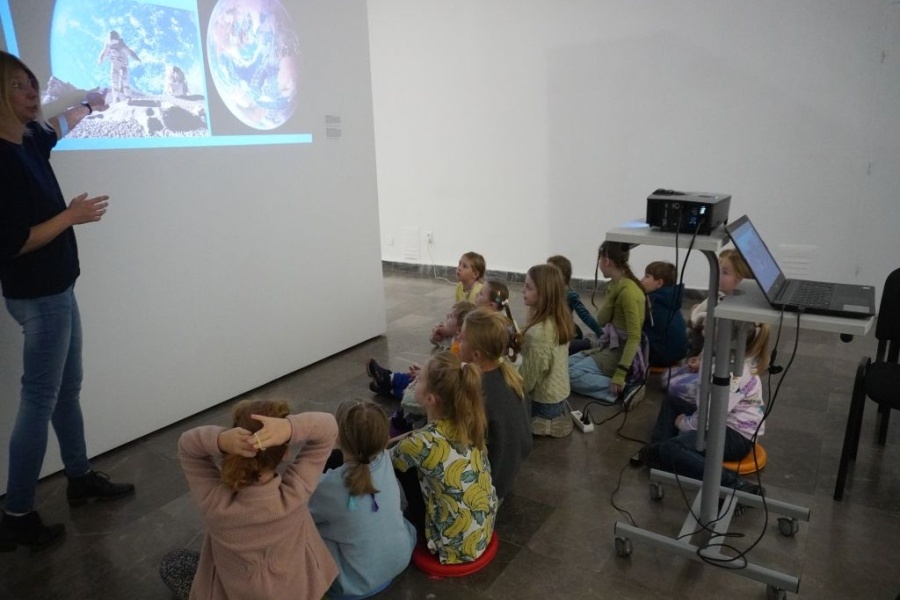 grupa dzieci ogląda prezentację na ścianie, przy niej stoi kobieta prowadząca zajęcia