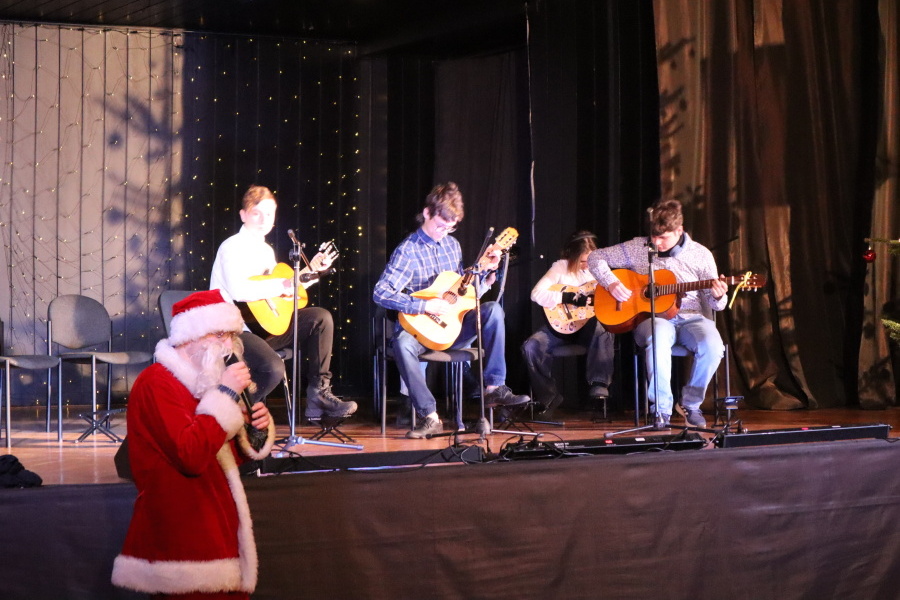 grupa uczestników z gitarami na scenie przed sceną Mikołaj z mikrofonem